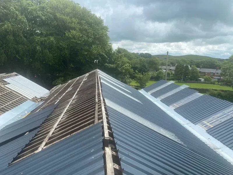 Multi-span roof part-way through re-sheeting, with new grey sheets either side of the exposed timber purlins at the ridge