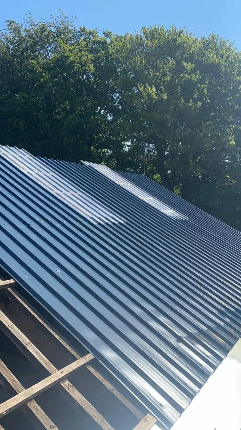 Freshly fixed dark grey profiled steel roof sheets with rooflights, next to an unsheeted bay